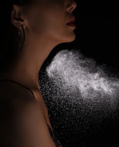 Woman spraying luxury perfume on black background, closeup