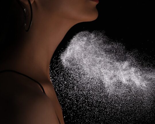 Woman spraying luxury perfume on black background, closeup
